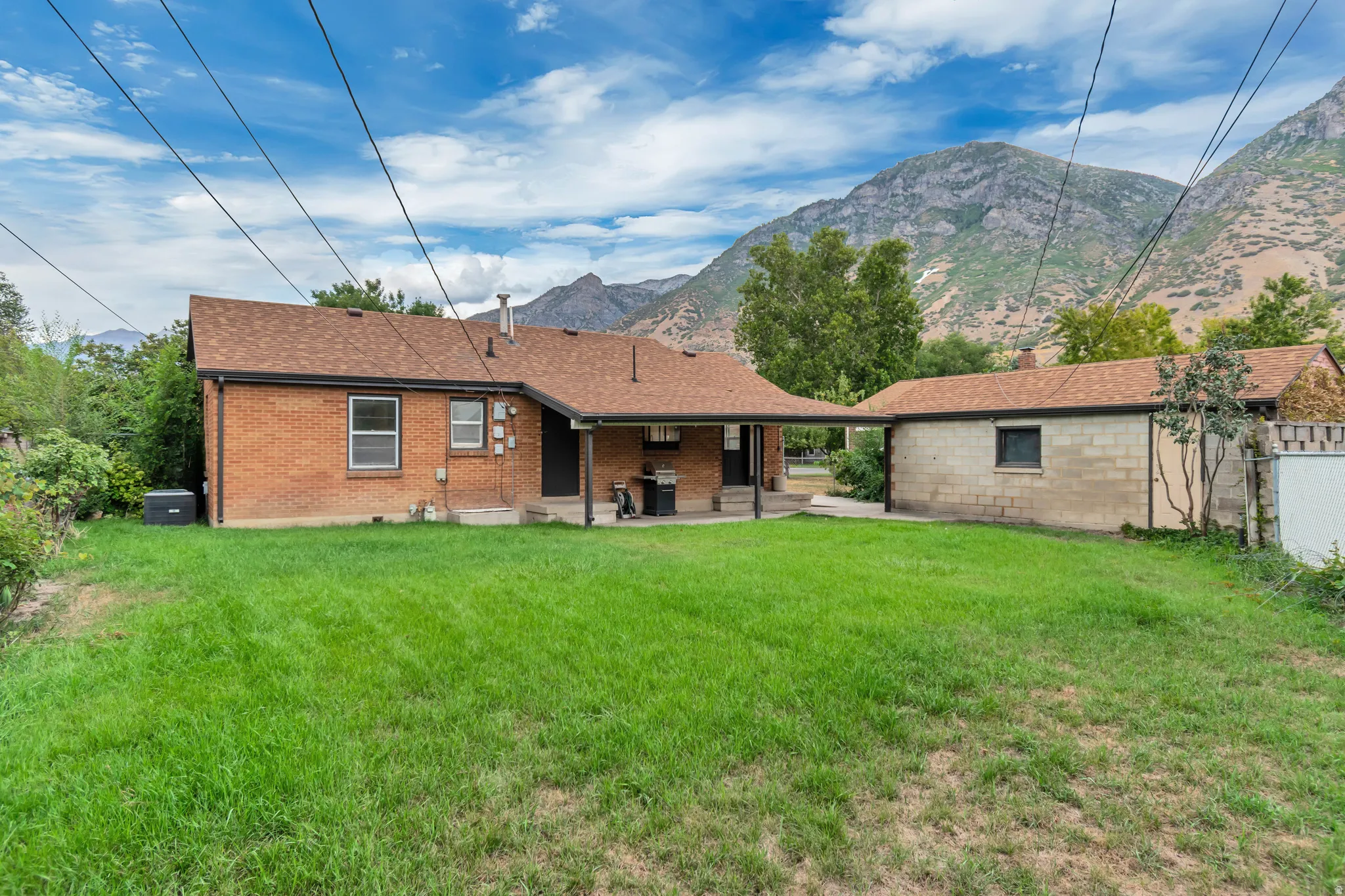 Brick exterior with a covered patio, detached structure, and expansive grassy yard
