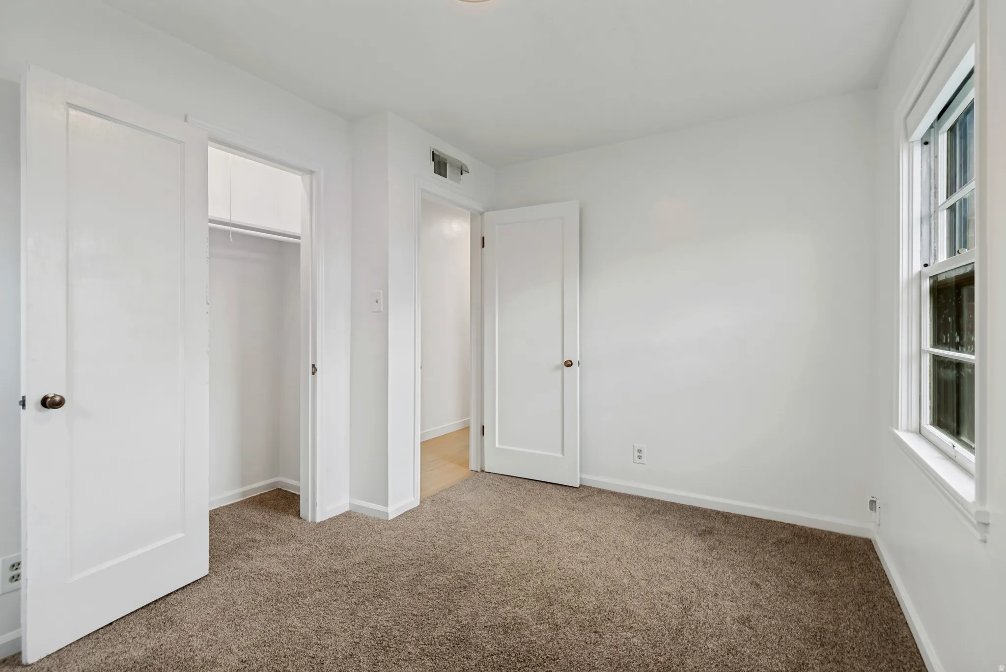 Spacious bedroom with neutral carpet flooring, abundant natural light from dual windows, and multiple closet options including a walk-in closet with shelving