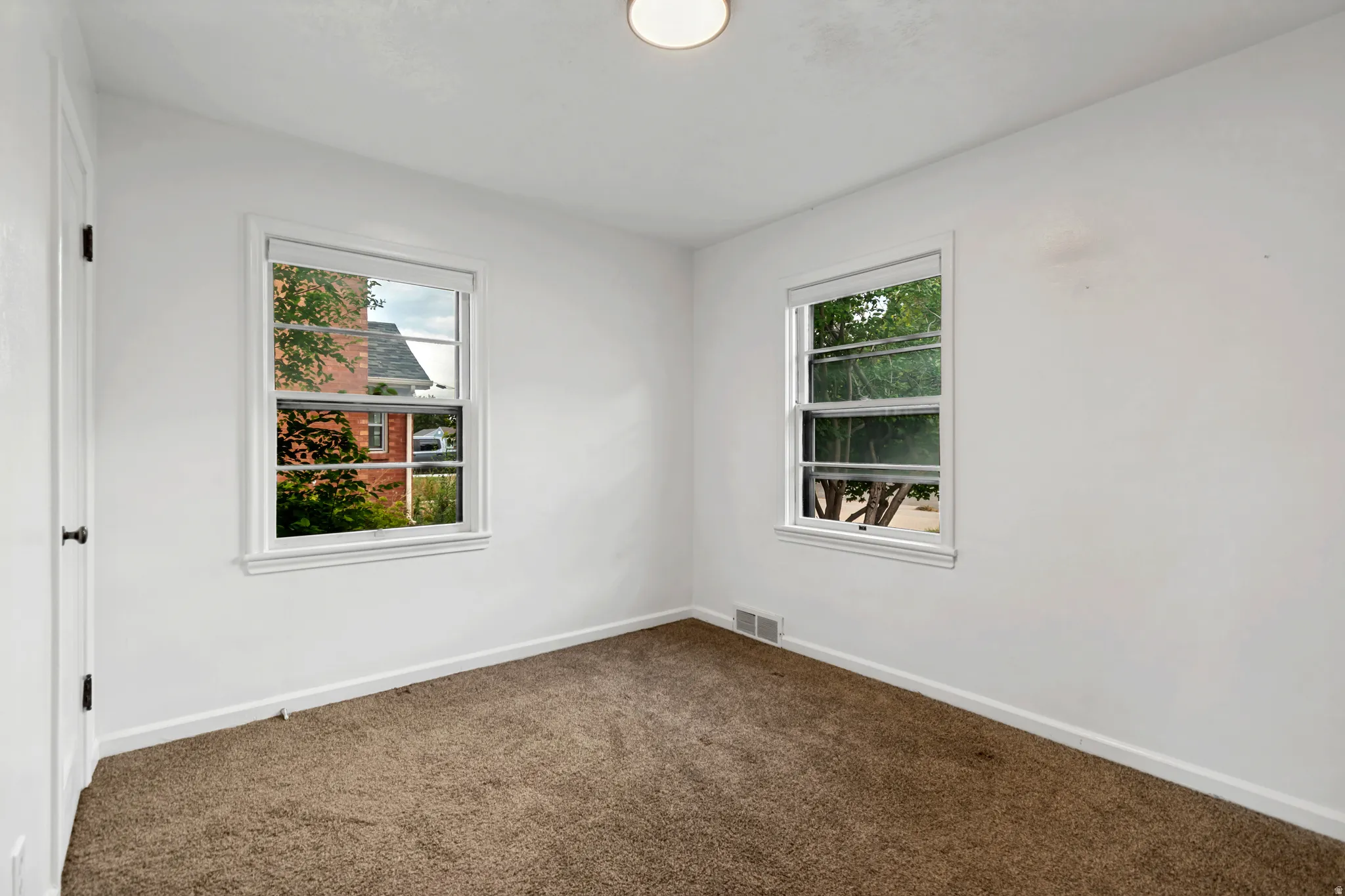 Bright corner bedroom with dual windows offering natural light, neutral wall finishes, and soft carpeting throughout