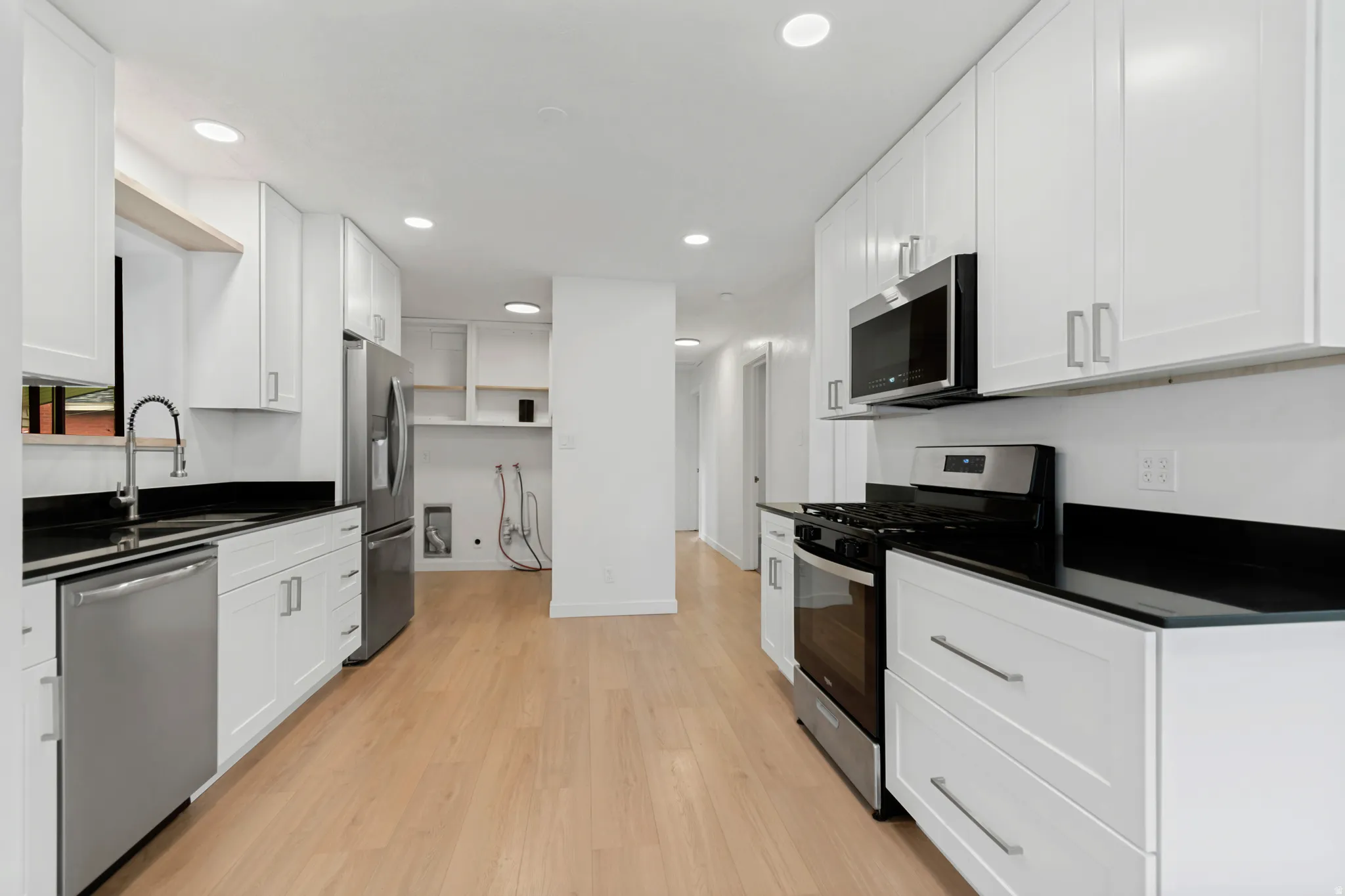 Kitchen featuring wood-finish flooring, white cabinetry, dark countertops, and stainless steel appliances