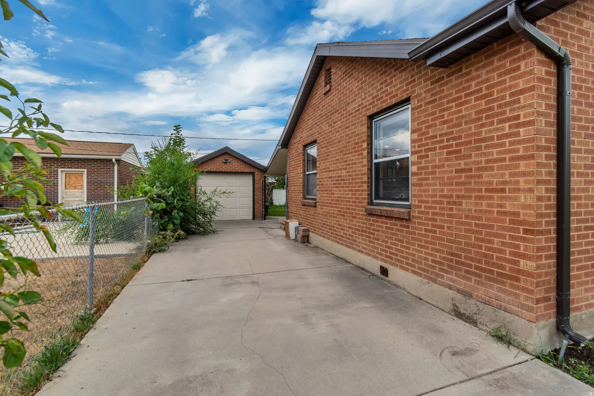 Brick exterior, concrete driveway, detached garage with overhead door, chain-link fencing, and dark gutters