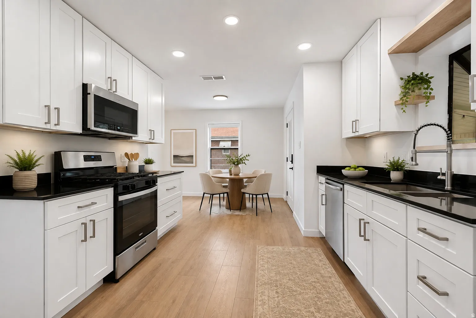 Galley-style kitchen featuring white cabinetry with stainless steel hardware, black quartz countertops, and stainless steel appliances including a slide-in range and microwave