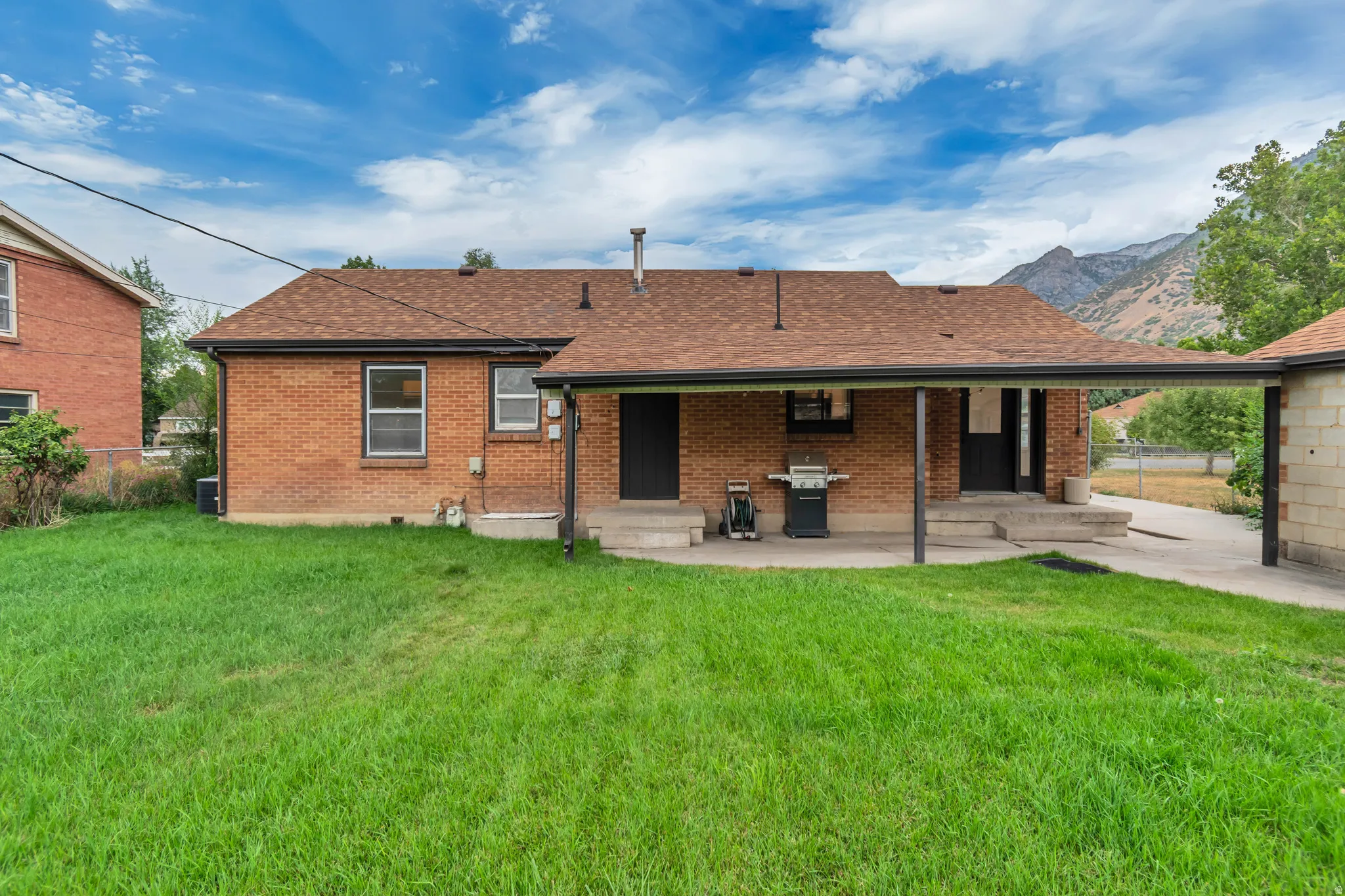 Brick Colonial home featuring a covered front porch, expansive manicured lawn, mature landscaping, attached garage, and mountain backdrop