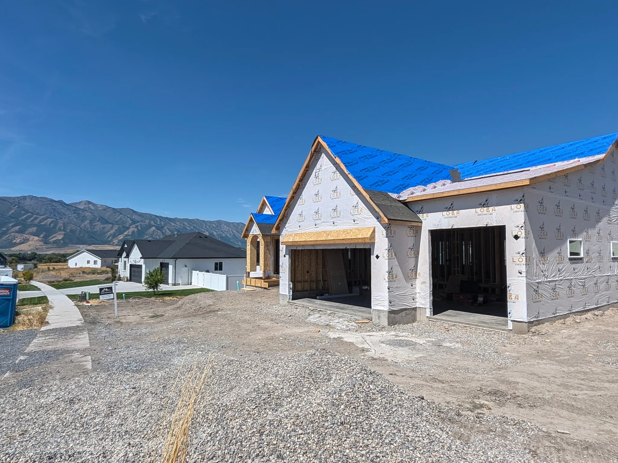 New construction featuring a distinctive peaked roofline with blue metal accents, white exterior cladding, and dark-stained wood entry doors