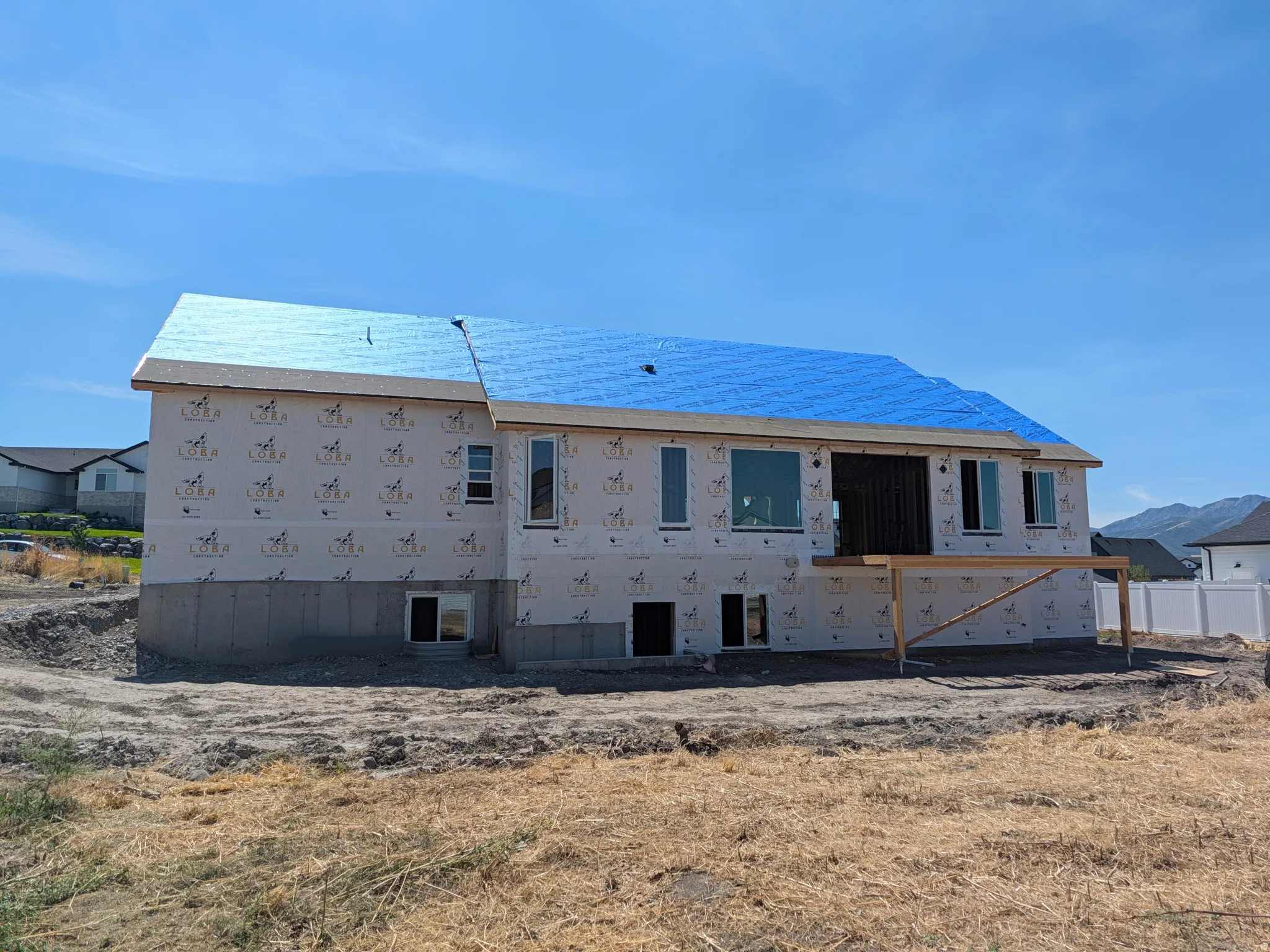 Newly constructed residence featuring a blue synthetic underlayment roof, multiple windows, a concrete foundation, and an unfinished deck structure