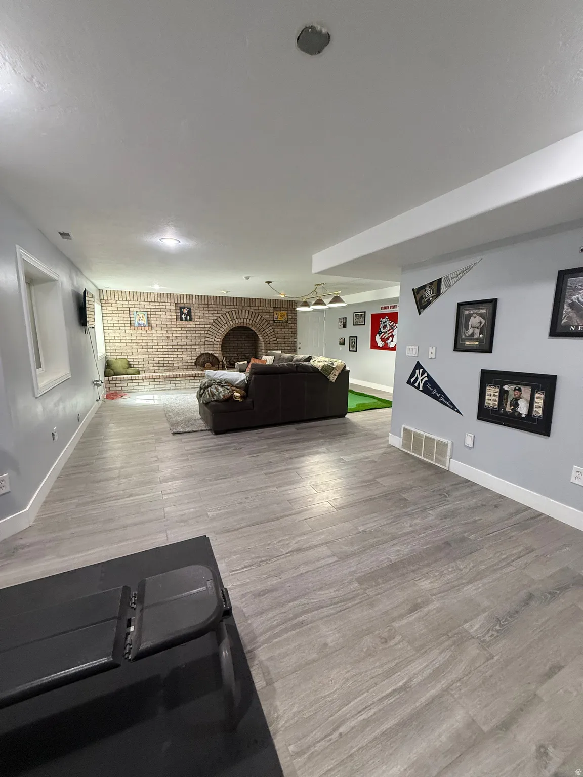 Spacious open-concept basement featuring wood-finish flooring throughout, recessed ceiling lighting, and a brick accent wall with arched architectural detail