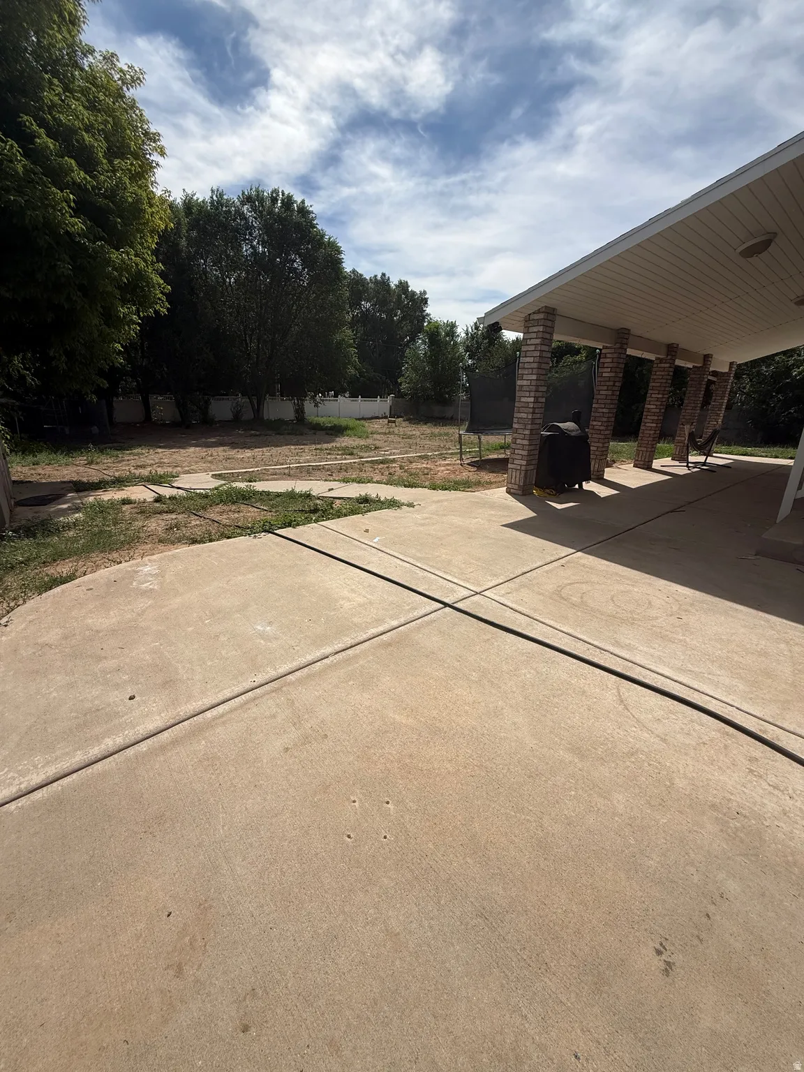 Expansive concrete patio with a covered outdoor area, brick-clad support columns, and a wide backyard with mature trees