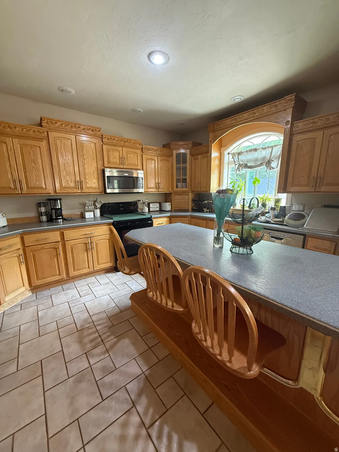 Kitchen featuring extensive wood cabinetry, an arched window, a built-in island with seating, a stainless steel microwave, and tile flooring
