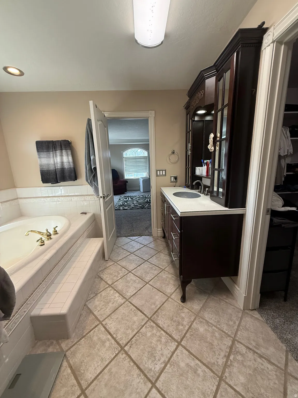 Built-in soaking tub with steps, dark wood-finish vanity with countertop sink, and diagonal tile flooring