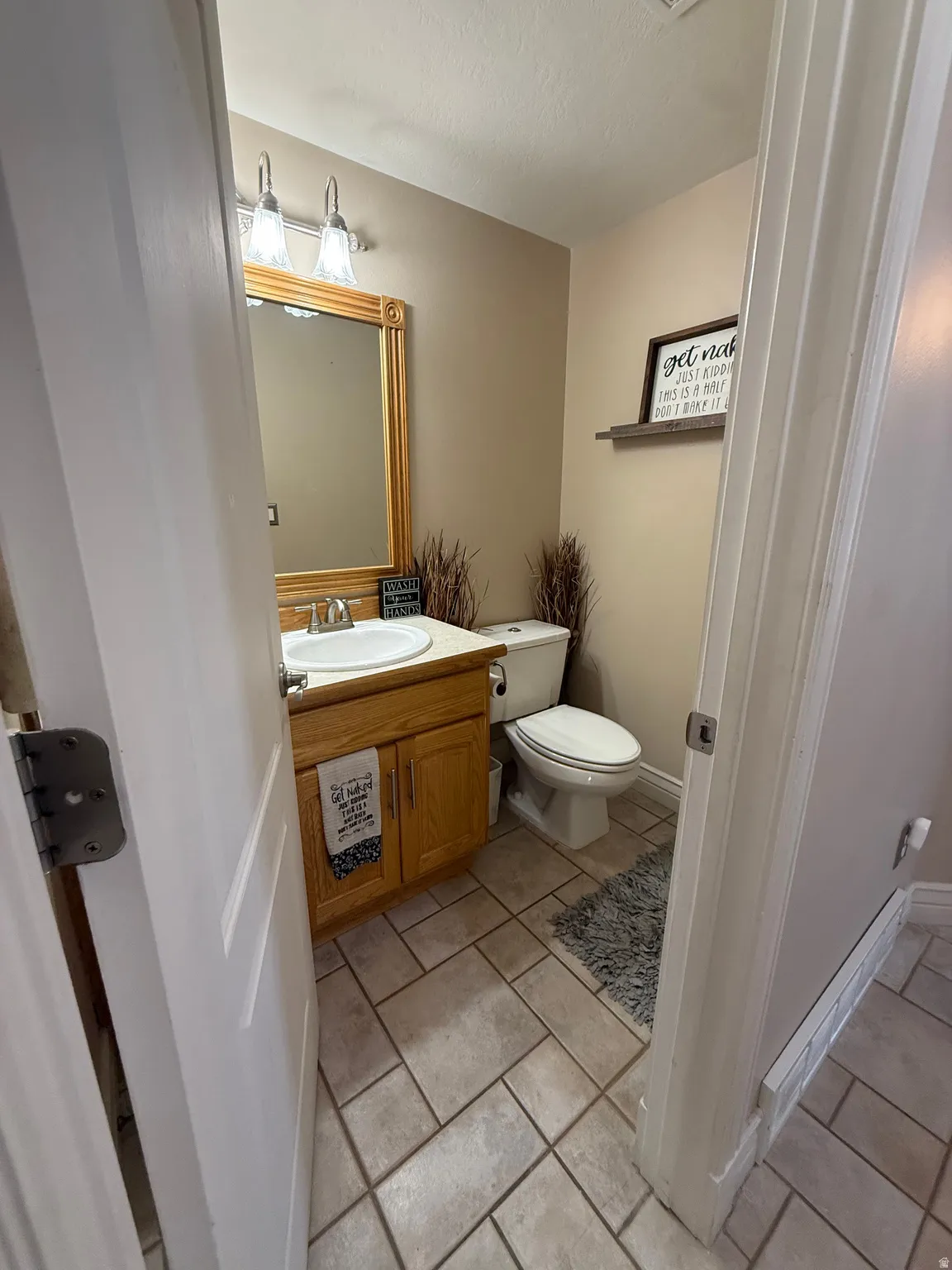 Tile flooring, wood-finish vanity with an integrated sink, wall-mounted light fixture, and a toilet