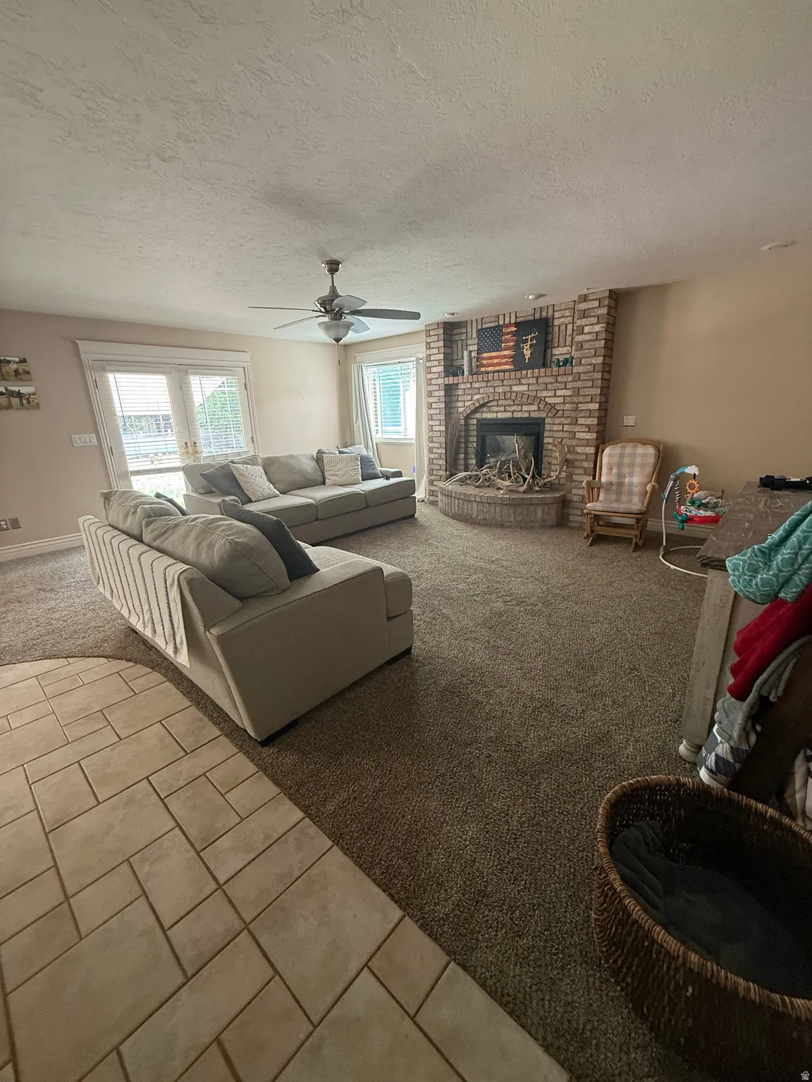 Brick-surround fireplace with hearth, ceiling fan, and carpeted flooring