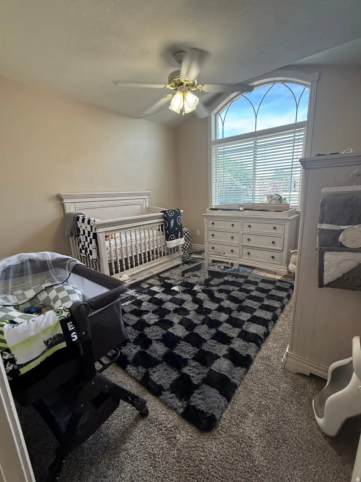 Arched transom window with blinds, vaulted ceiling, ceiling fan with light fixture, and carpet flooring