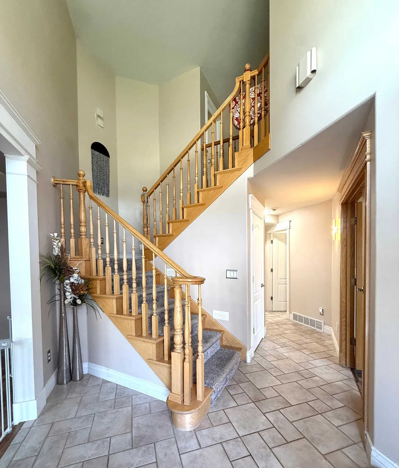 Grand entryway with a two-story ceiling, natural wood staircase, carpeted stair runner, tile flooring, and decorative wall sconces