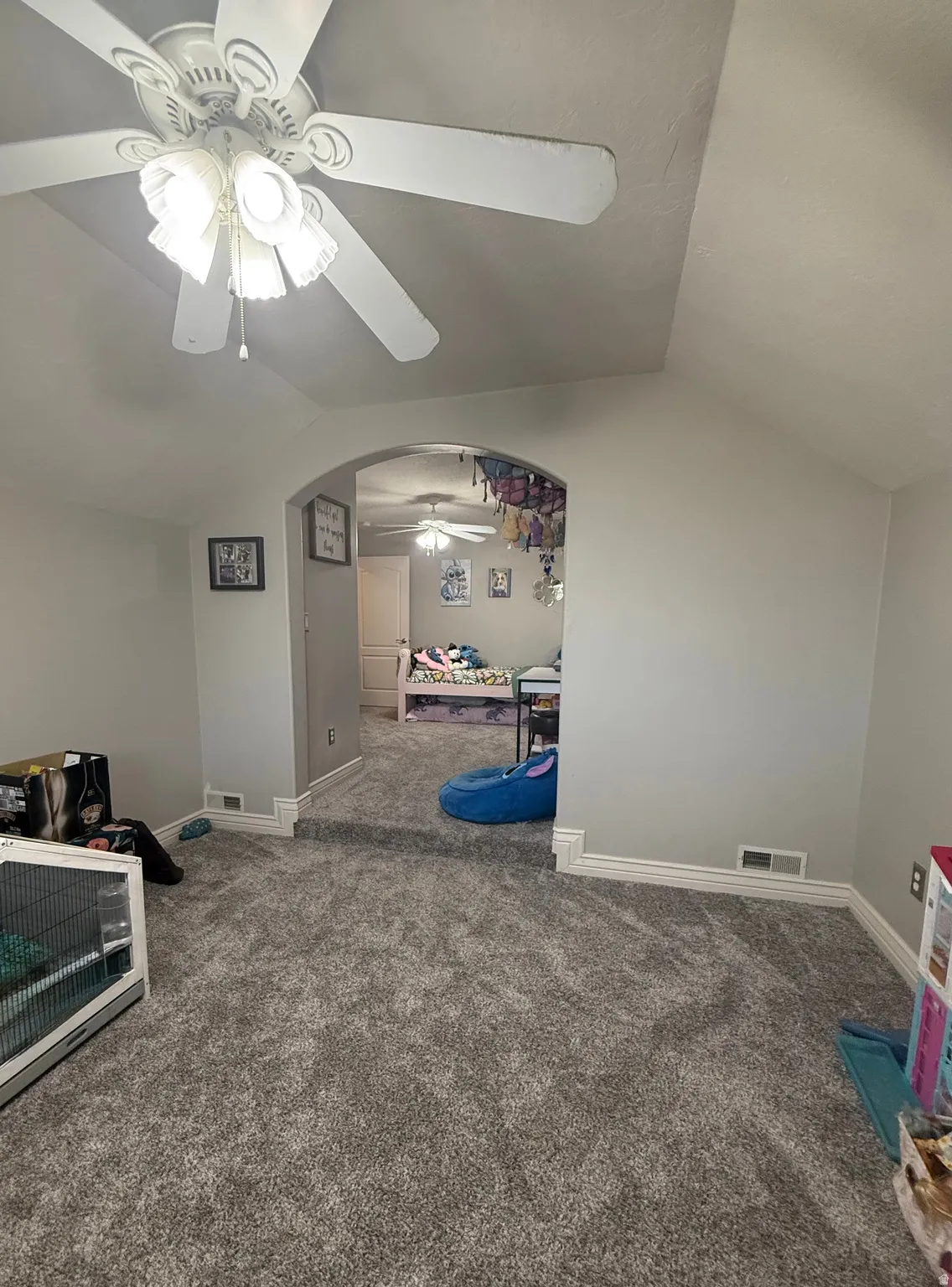 Arched entryway with a step-up transition, gray carpeting, and a ceiling fan with integrated lighting