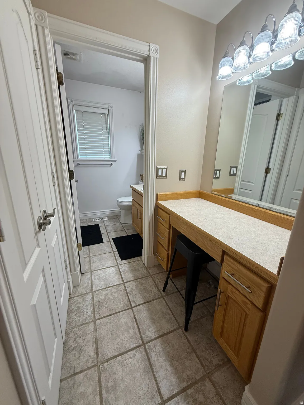 Tile flooring, vanity with wood-finish cabinetry, built-in mirror, and a multi-bulb light fixture