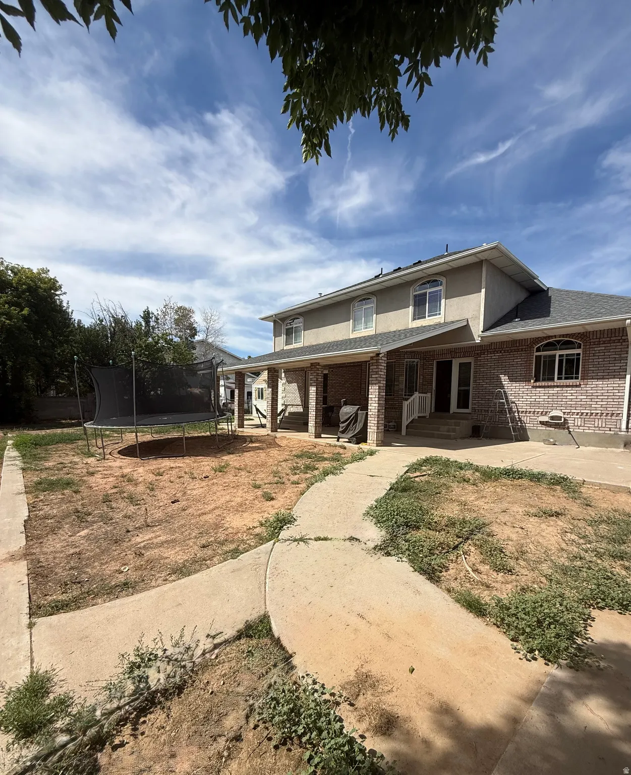 Rear exterior with brick and stucco facade, arched windows, covered patio, and concrete pathway