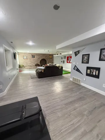 Spacious open-concept basement featuring wood-finish flooring throughout, recessed ceiling lighting, and a brick accent wall with arched architectural detail