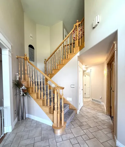 Grand entryway with a two-story ceiling, natural wood staircase, carpeted stair runner, tile flooring, and decorative wall sconces