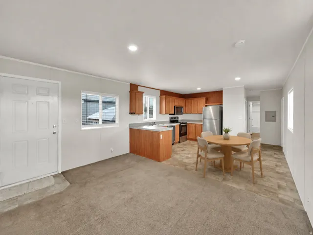 Open-concept kitchen and dining area featuring wood-finish cabinetry, stainless steel appliances, laminate countertops, and a centered island with seating