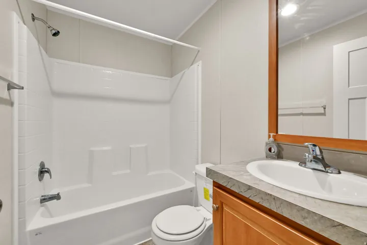 Integrated tub and shower combination, vanity with an undermount sink, wood-finish cabinetry, and a framed mirror