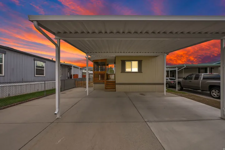 Covered carport, light-colored siding, dark trim, concrete driveway, and a wood porch with railing