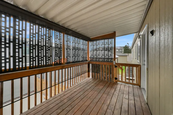 Covered outdoor deck featuring wood-finish flooring, wood-finish railings, and decorative metal privacy screens