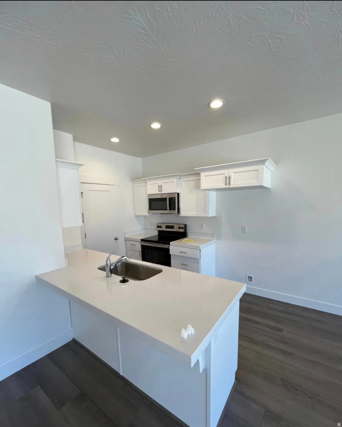 White shaker cabinetry with stainless steel appliances, wood-finish flooring, recessed lighting, and a kitchen island with an undermount sink