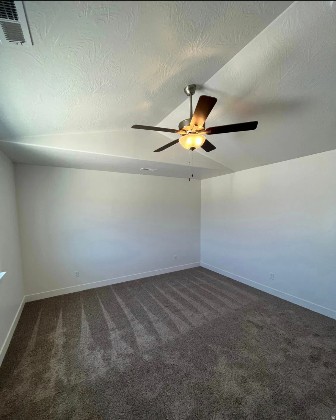 Vaulted ceiling with textured finish, ceiling fan with integrated lighting, broadloom carpet flooring, and white wall finishes