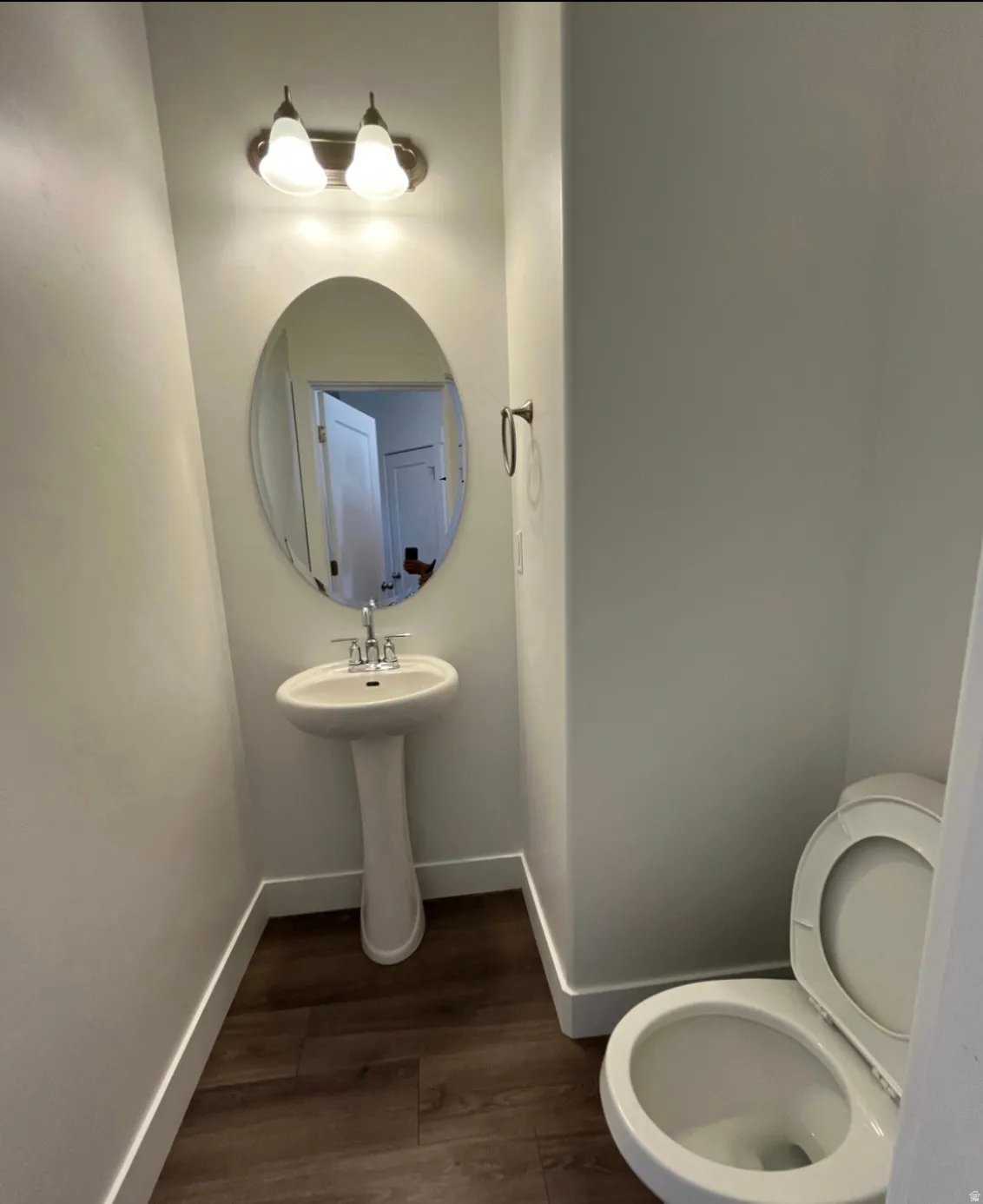 Pedestal sink with chrome fixtures, oval mirror, and a two-bulb vanity light fixture