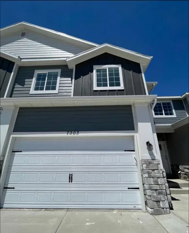 Multi-level exterior with mixed siding, stone veneer accents, and a panel garage door