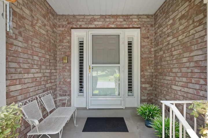 Brick facade entry featuring a full-light storm door, sidelight windows, and a white ceiling