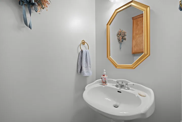 Pedestal sink with chrome faucet, octagonal framed mirror, and brass-tone towel ring