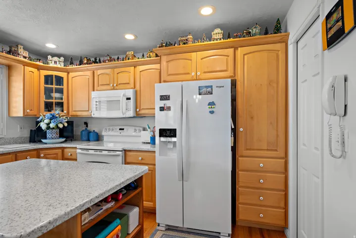 Wood-finish cabinetry, recessed lighting, white side-by-side refrigerator, white built-in microwave, and wood-finish flooring