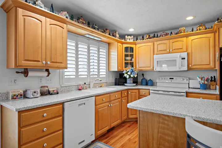 Kitchen featuring wood cabinetry, light-toned countertops, a white built-in microwave, white range, and wood-finish flooring