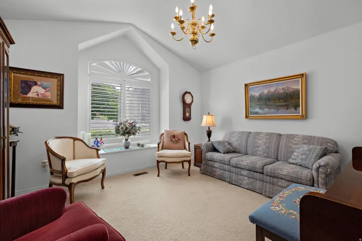 Vaulted ceiling with a brass chandelier, arched window with plantation shutters, and a wall-mounted clock