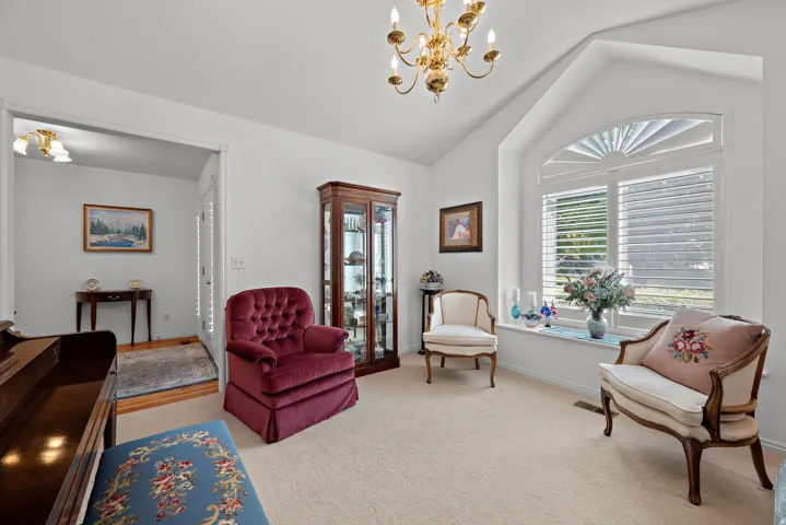 Vaulted ceiling with an ornate chandelier, arched window with plantation shutters, and light-colored carpeting