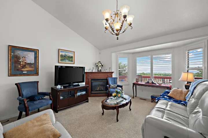 Bright and spacious living room featuring vaulted ceilings, a decorative chandelier, expansive windows with plantation shutters, and hardwood cabinetry with built-in entertainment storage