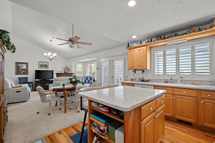 Vaulted ceilings with recessed lighting, kitchen island with stone countertop, wood-finish cabinetry, hard surface flooring, and plantation shutters
