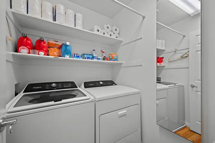 Laundry area with white walls, two white appliances, built-in shelving, a hanging rod, and a partial mirror