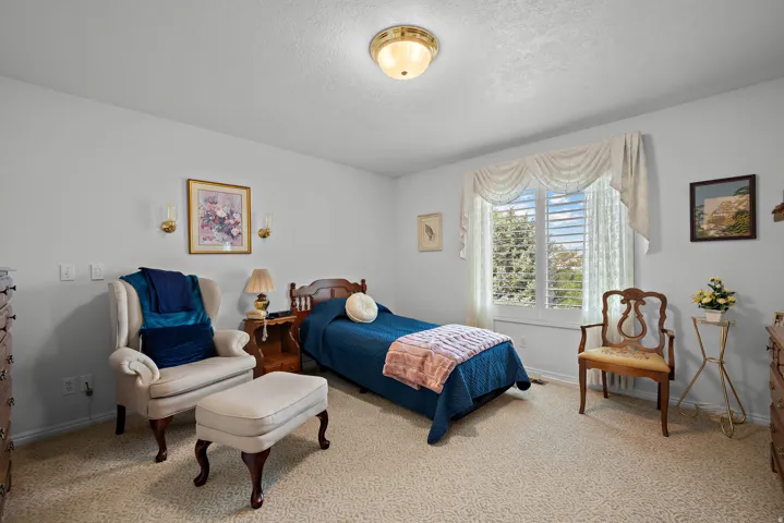 Wall-to-wall carpeting, window with plantation shutters, overhead flush-mount lighting, and wall-mounted sconces