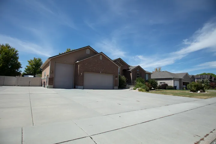 Brick and stucco exterior with multiple garage doors, concrete driveway, and established landscaping