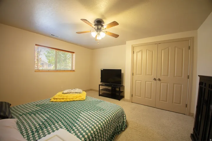 Wall-to-wall carpeting, window with wood-finish blinds, double bi-fold closet doors, and a ceiling fan with integrated lighting