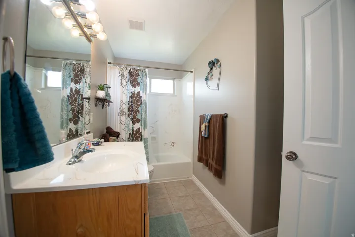 Spa-inspired bathroom featuring a wood-finish vanity with an integrated sink, ceramic tile flooring, and a combined shower-tub enclosure with decorative tile surround