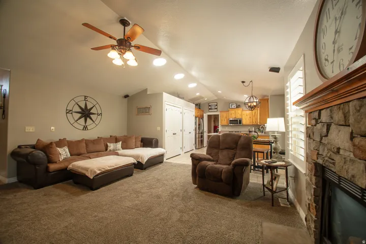 Recessed ceiling lighting, wood-finish ceiling fan, stone-clad fireplace with wood mantle, plantation shutters, and wood-finish kitchen cabinetry
