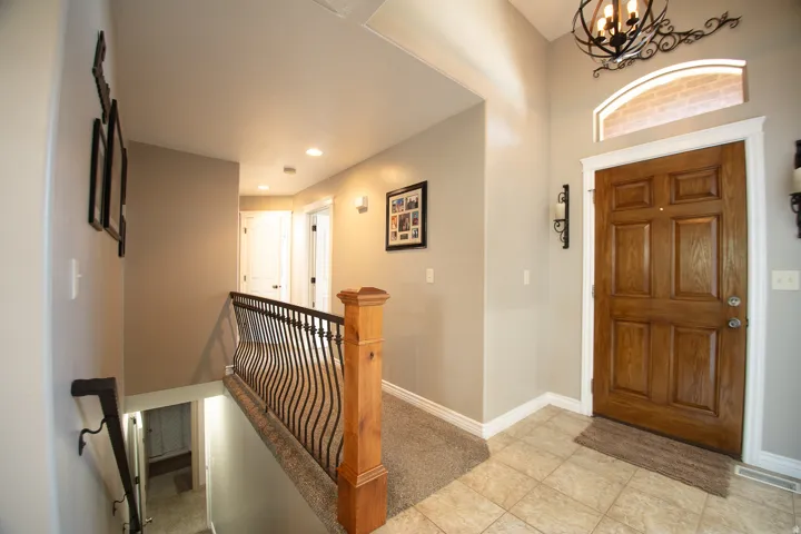Wood paneled front door with arched transom window, tile flooring, wrought iron staircase railing, and recessed lighting