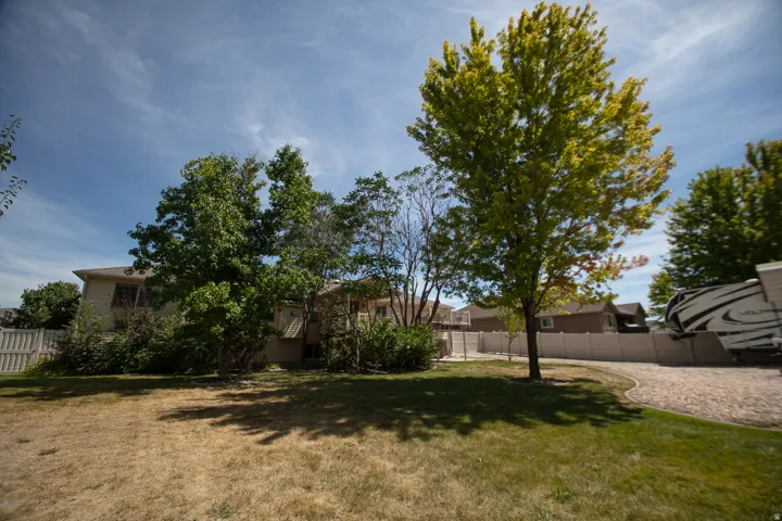 Expansive yard featuring mature trees, a gravel parking area, and a privacy fence