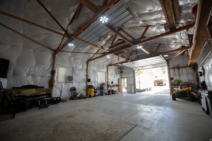 Spacious interior with exposed wood beam ceiling, concrete flooring, multiple windows, and a large roll-up garage door