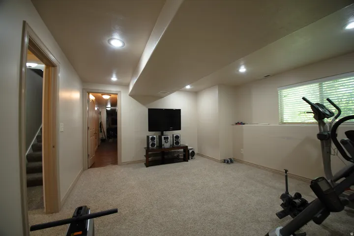 Recessed lighting, light beige carpeting, window with blinds, light wood-finish door frames, and white painted walls