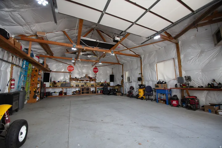 Open garage space with exposed wood beams, concrete flooring, and ample overhead lighting