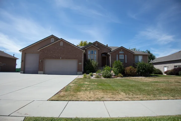 Brick exterior with a stucco accent, multiple garage doors, a concrete driveway, and front landscaping